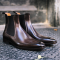 Pair of brown leather Chelsea boots on a textured surface with a blurred background